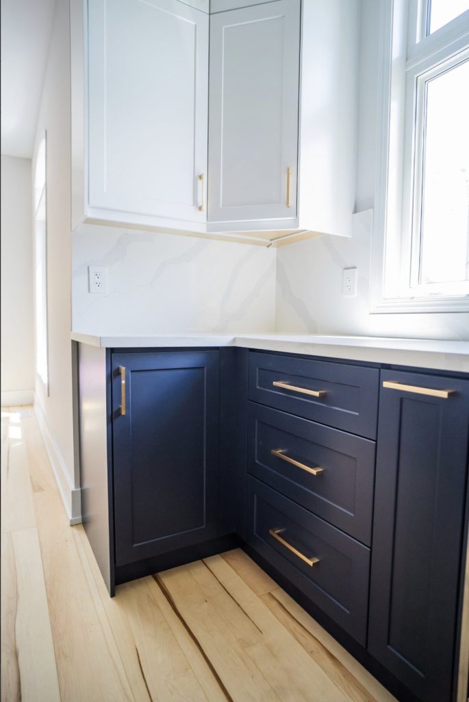 Navy lower cabinets with brass pulls under a marble backsplash